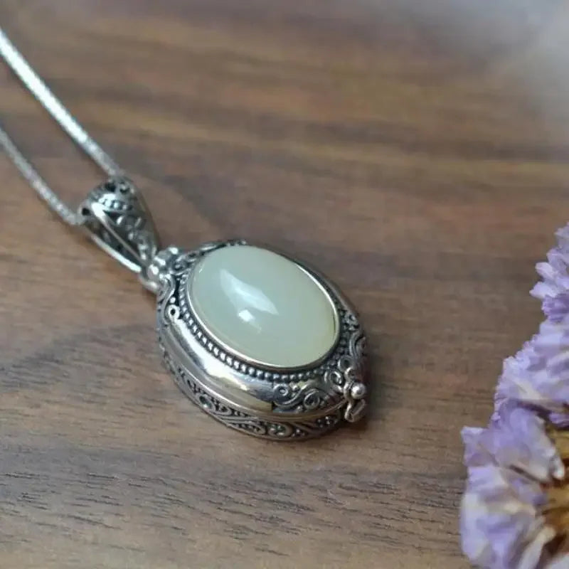 Oval locket necklace in White, milky stone in an ornate silver-tone frame on a wooden table