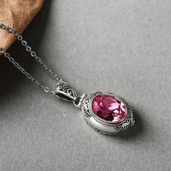 Oval locket necklace in Pink, pink stone in an ornate silver-tone frame on grey stone