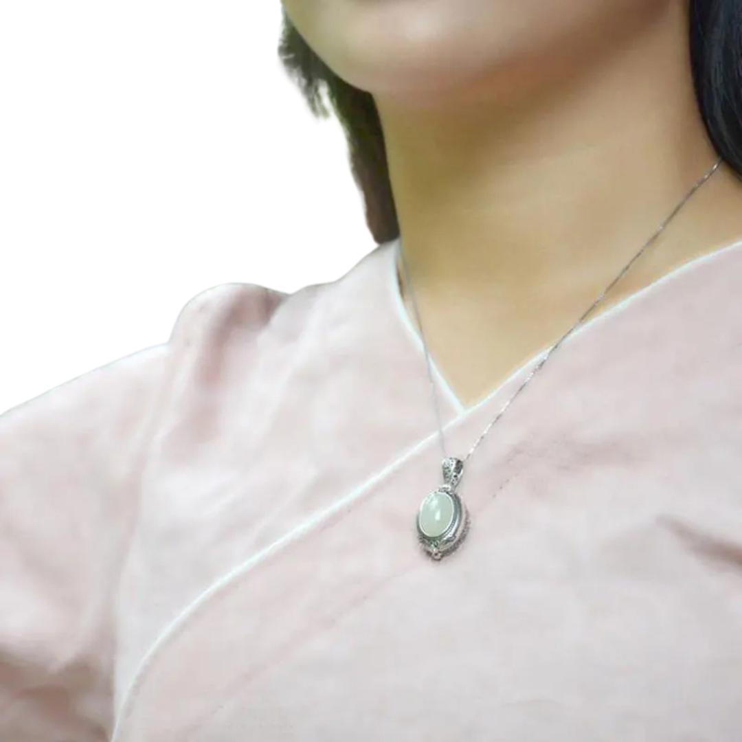 Oval locket necklace worn on a silver-tone chain against a pale pink top